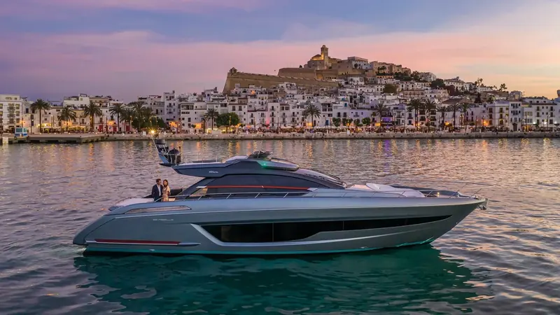 At anchor off Ibiza's Dalt Vila at dusk, the coupe's silhouette against a working harbour town shows the scale the Ribelle is built to be seen at.