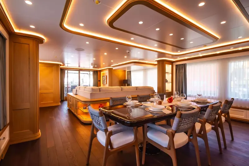 The main saloon dining table aboard Seven Seas, seating eight beneath a lit ceiling coffer