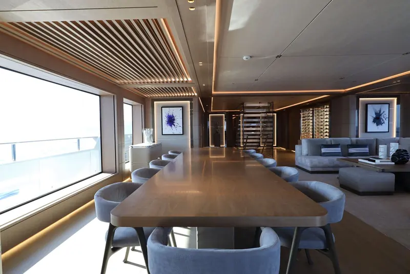 The main-deck dining table seats ten beneath a slatted timber ceiling, with the adjoining lounge kept open-plan rather than screened off, so the whole deck reads as one room.