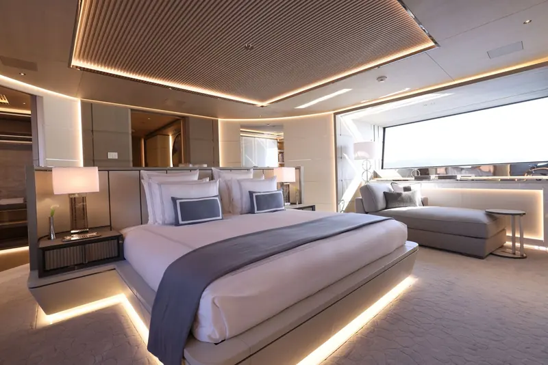 The master suite runs the full beam with backlit joinery framing the bed and a separate seating area to starboard, lit almost entirely by concealed LED coves rather than downlights.