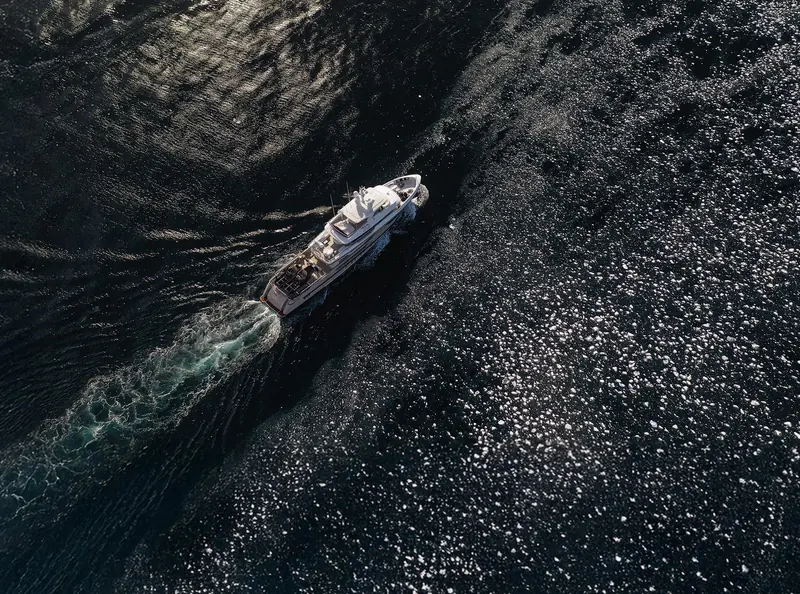 An aerial view cutting a wake through sea ice shows the hull's displacement-style waterline and the tender-launch deck aft, cleared for the crane and toy stowage the explorer brief calls for.