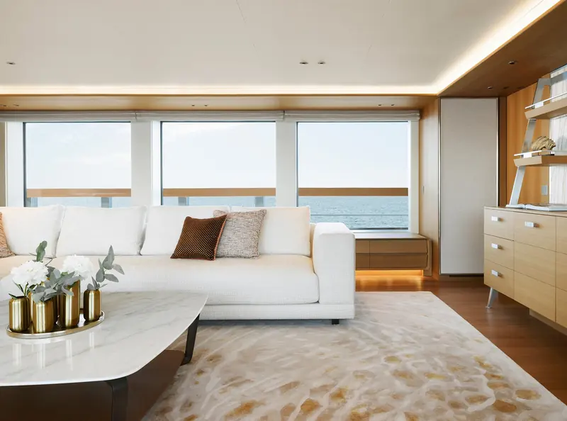 A main-deck saloon in a pale oak and white palette, one of several 500EXP interiors by Studio Indigo built around full-height glazing rather than the traditional dark-timber explorer look.