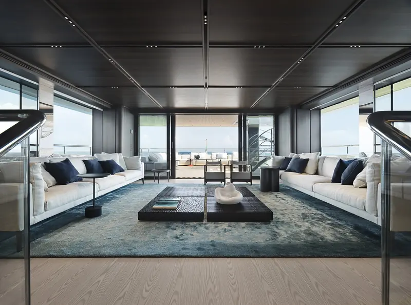 The main-deck saloon, twin cream sofas around a dark stone coffee table, opening aft to the deck and the sea beyond.