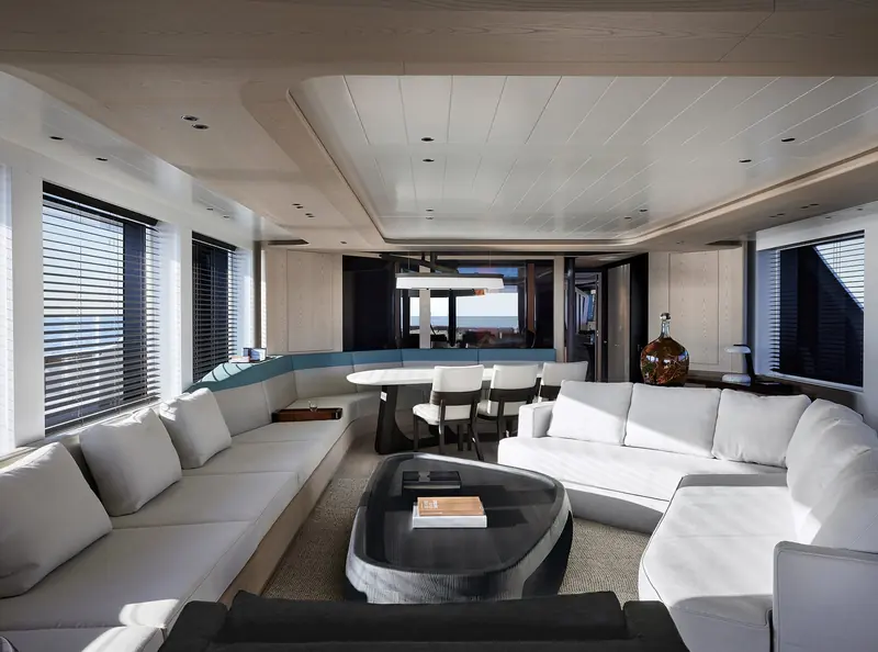 Liaigre's main salon uses a single wraparound sofa and a free-standing oval dining table rather than the fixed banquettes common at this size, with venetian blinds controlling the light off the water.