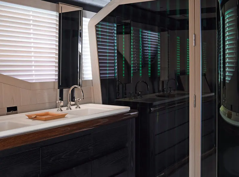 An en-suite bathroom pairs a dark wood vanity with white stone counters, one of several material contrasts Liaigre used to keep the interior from reading as one uniform pale box.