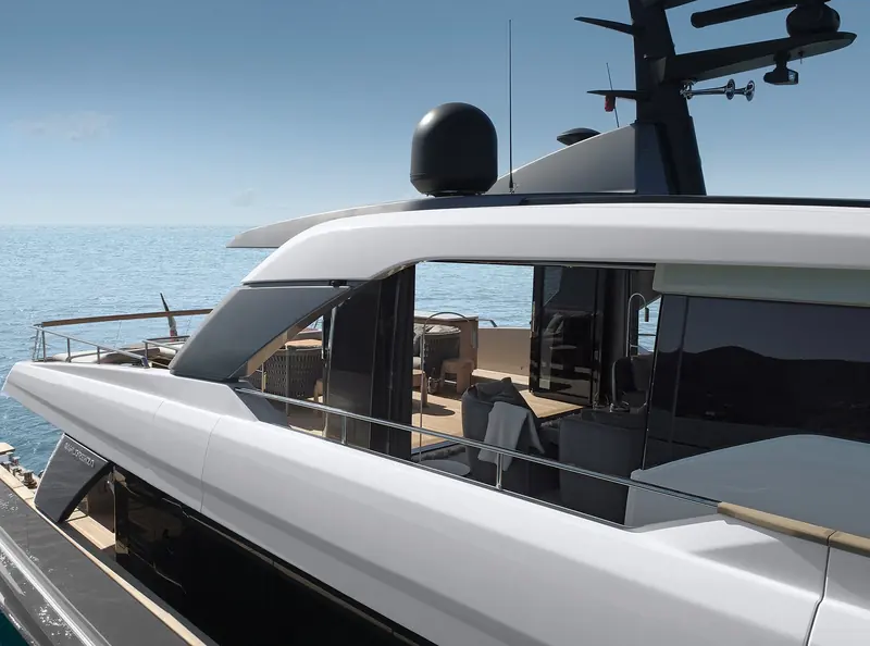 The flybridge lounge is glazed on three sides, its black window glass throwing back the shoreline of the anchorage rather than the sky.