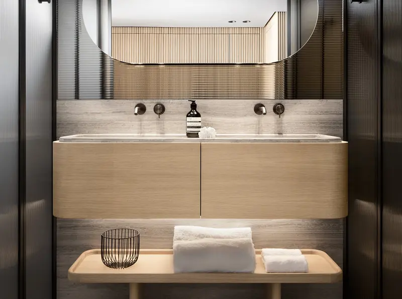 The ensuite's double-width vanity is lit from a top-hung mirror rather than side sconces, keeping the fittings below it uncluttered.
