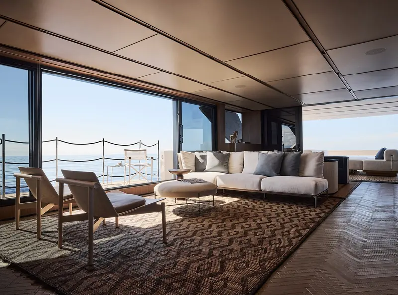 The main-deck saloon opening onto the side deck, herringbone flooring and a sectional sofa.