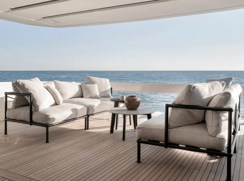 An aft-deck lounge with black-framed outdoor furniture under an open sky.