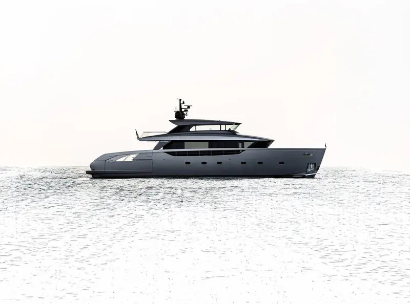 The Sanlorenzo SX100 at rest on a mirror-calm sea, the crossover hull's distinctive dark upper deck against a white hull.