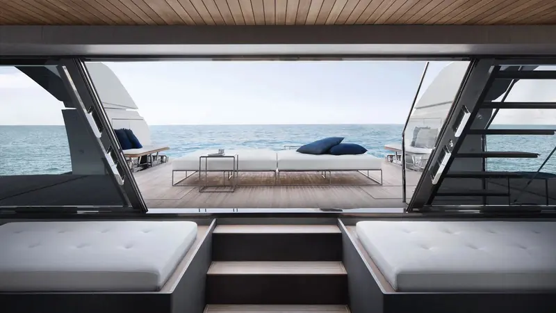 Looking aft through the open beach club doors from the lower-deck lounge, with twin daybeds set either side of a folded glass panel and the aft deck sunpad visible beyond the transom.