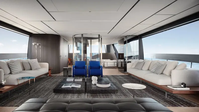 The main-deck saloon, dressed by Piero Lissoni with cobalt-blue armchairs against pale linen sofas and a smoked-glass lift shaft standing where a conventional stair would normally interrupt the room.