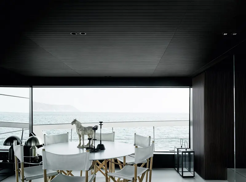 The main-deck dining area, black joinery and a round table looking straight out to sea.