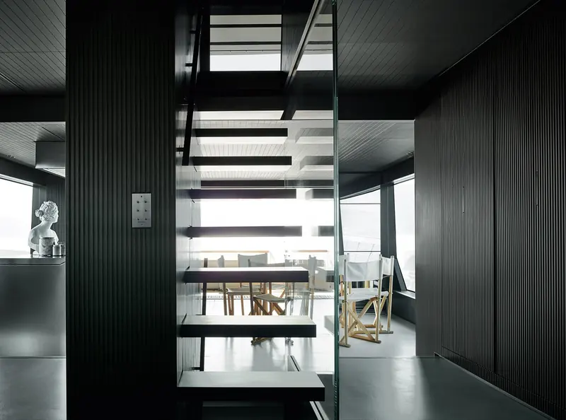The internal staircase connecting decks, glass balustrade against black panelling.