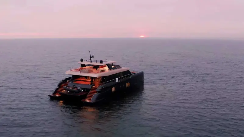 The catamaran silhouetted against a pink dusk sky, hull profile low and wide on the water.