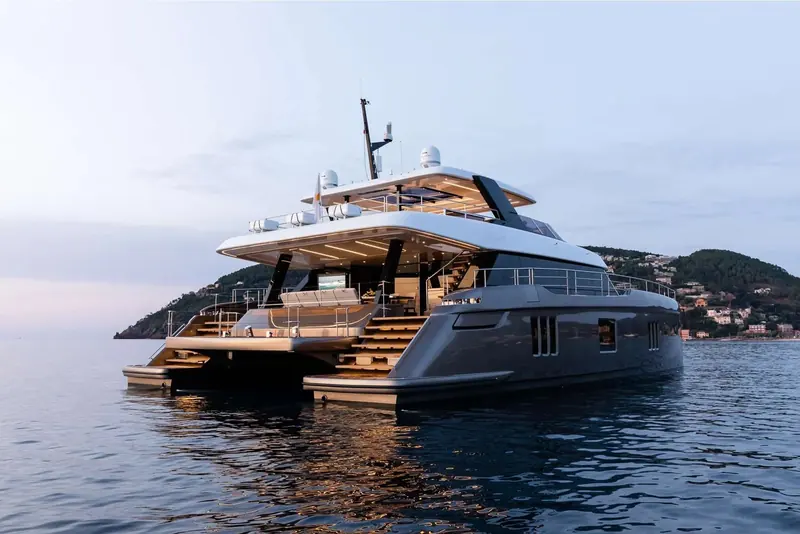 The catamaran at anchor off a wooded coastline, aft platforms lowered at the stern.