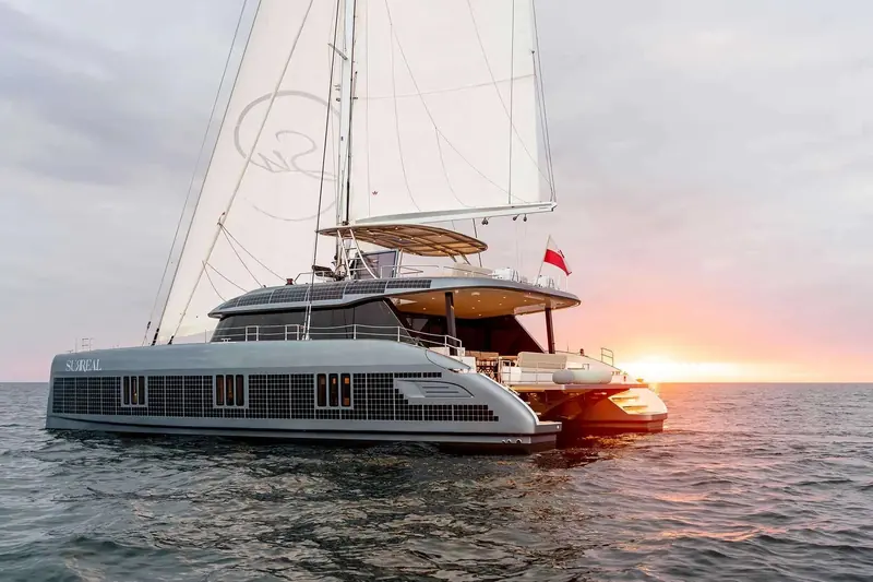 The Sunreef 60 Eco, hull name Surreal, sailing at sunset with her code sign and solar-cell topsides lit by the low sun.