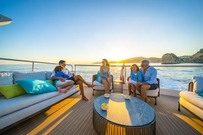 A family gathered on the flybridge sunpad at dusk, the informal, low-key styling Sunseeker uses for its own photography rather than a staged brochure shot.