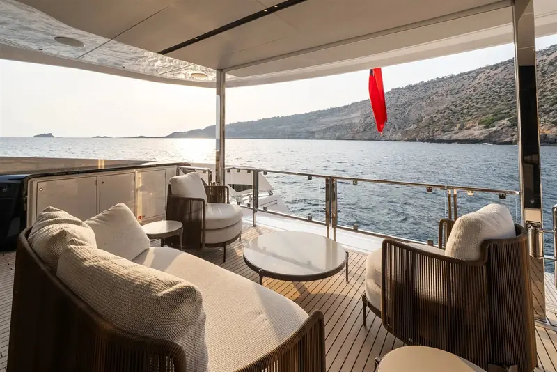 The covered aft deck lounge seats a full dinner party in the shade of the flybridge overhang, with woven furniture set for sundowners.