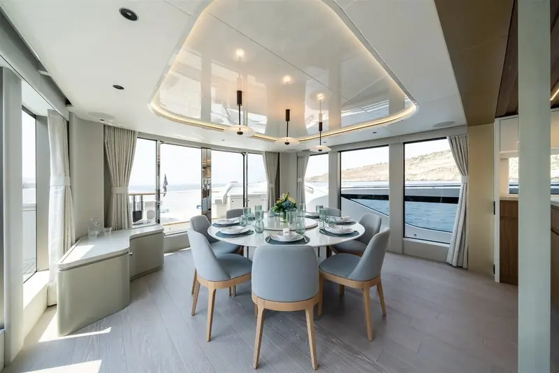 The enclosed dining saloon seats six under a sculpted ceiling detail, glazed on three sides so the anchorage stays in view through the meal.