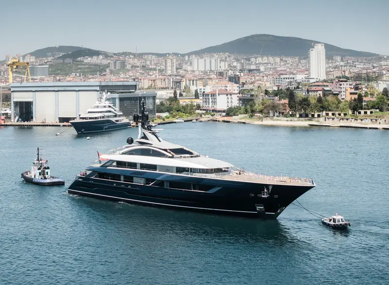 A wider harbour view sets the yacht against Istanbul's skyline, with a sister black-hulled Turquoise yacht still fitting out in the shed behind.