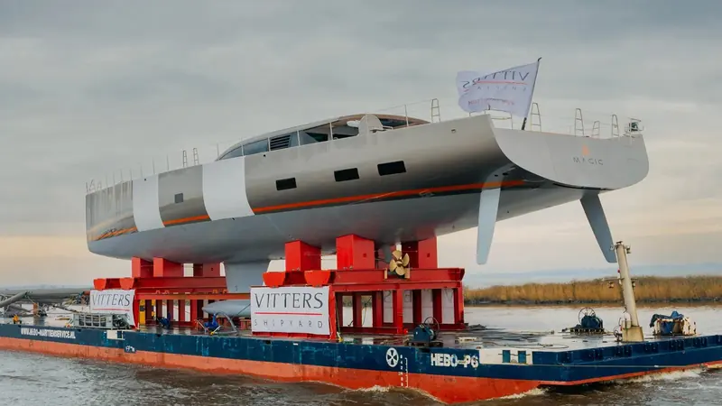 Magic's hull is transported by barge from the Vitters build shed ahead of launch.