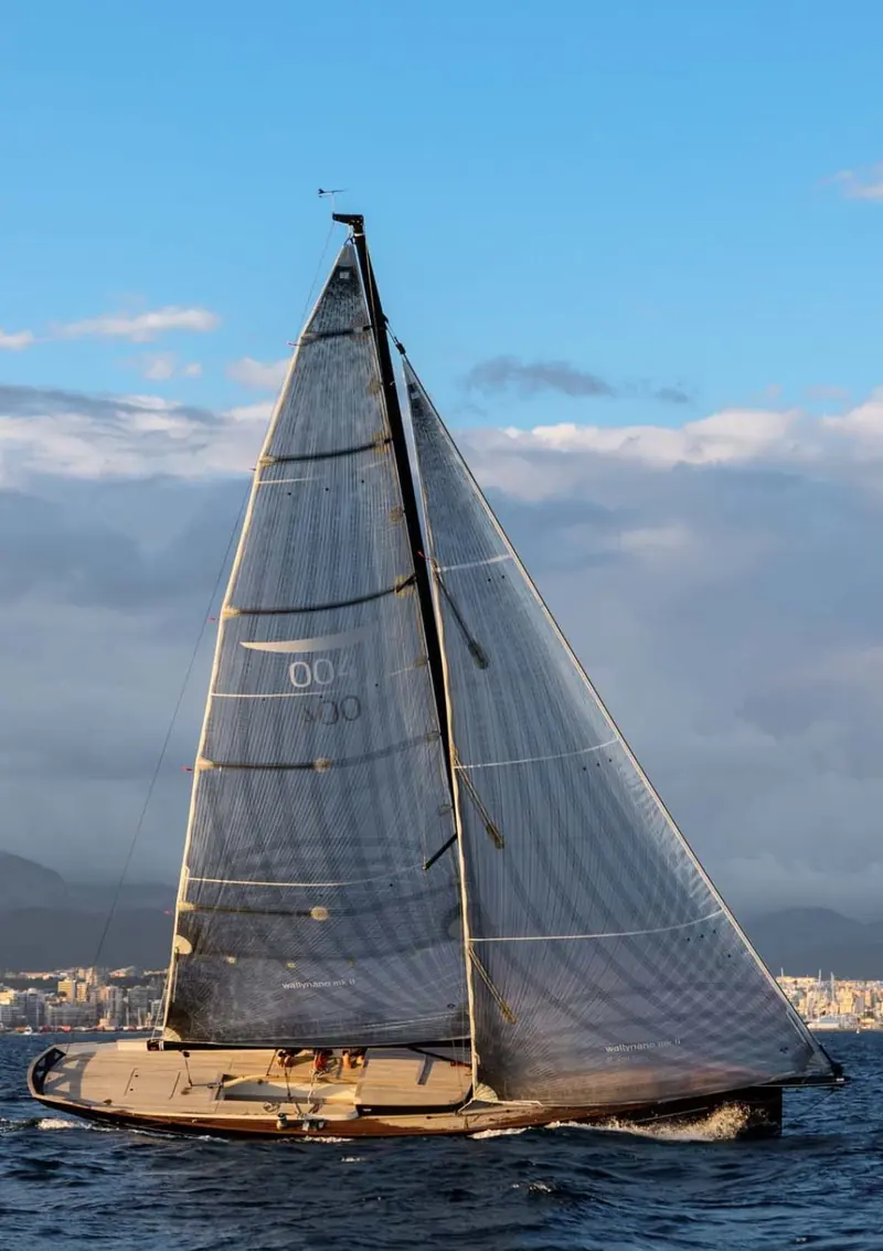 Sailing solo-handed in evening light, the boat carries no deck hardware forward of the mast beyond what one person needs to reef and tack alone.