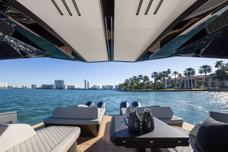 Aft cockpit seating and a fold-out table sit under the hardtop overhang, with the Miami waterfront visible over the transom at anchor.