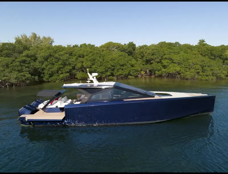 Bow-on past a mangrove shoreline, the reverse bow and stepped hull sides throwing spray clear of the deck.