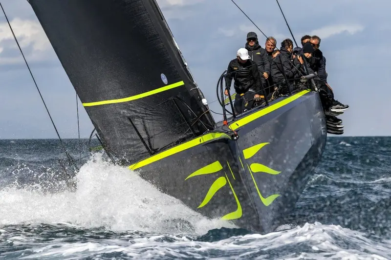 Bow-on close as the crew works the rail mid-tack, the twin daggerboard cases visible either side of the black hull.