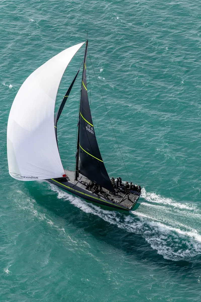 Running downwind under a white gennaker set against the mainsail, the fluorescent yellow hull striping catching the light.
