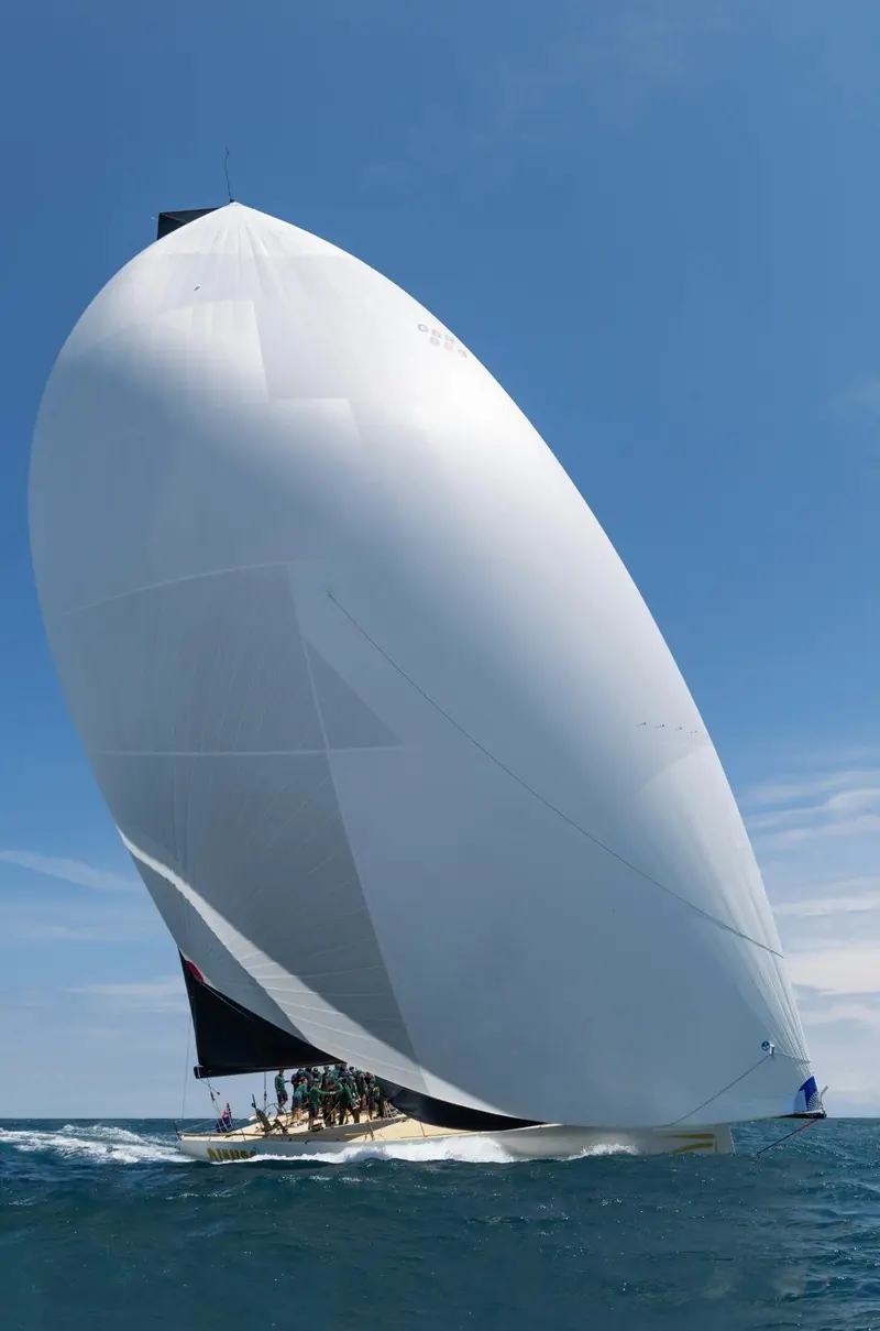 Running downwind under a full white spinnaker, the black mainsail blanketing behind it against a clear sky.