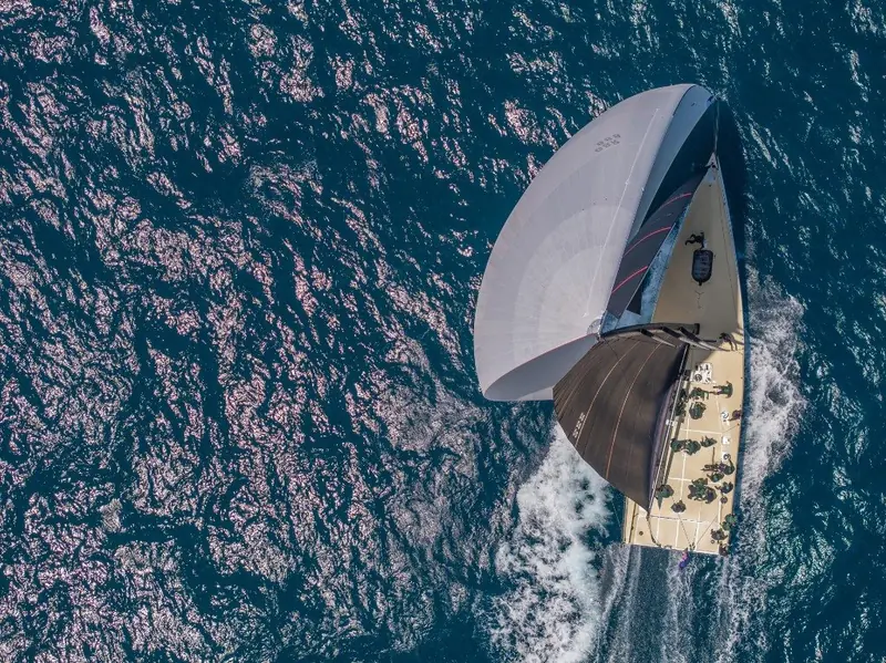 Overhead view of the spinnaker filled and the crew working the foredeck, the sail's curvature showing the boat's downwind power.