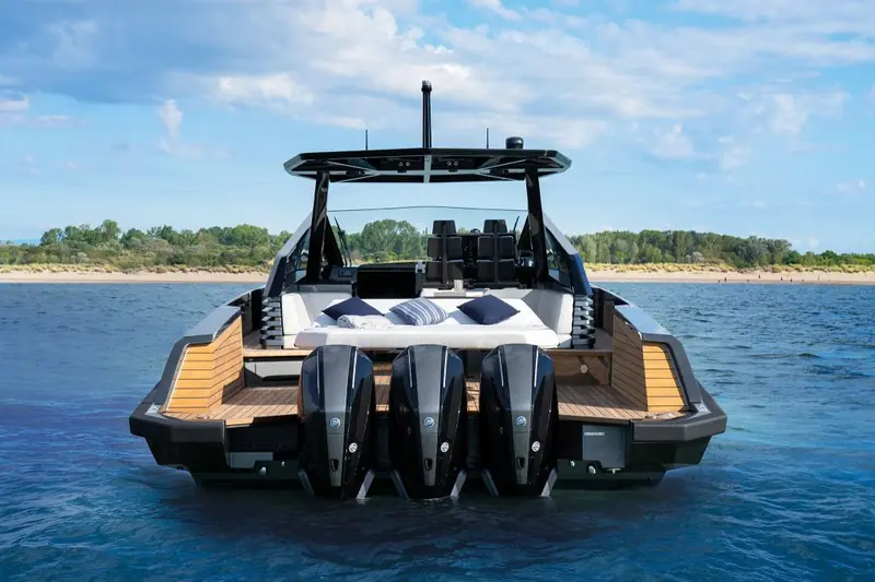 Stern-on at anchor off a wooded shoreline, sunpad cushions set out on the foredeck and outboards trimmed down.