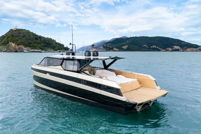 Underway at a fast cruise off a mountainous stretch of coast, helmsman visible at the wheel and the low, dark-glazed superstructure catching the light.