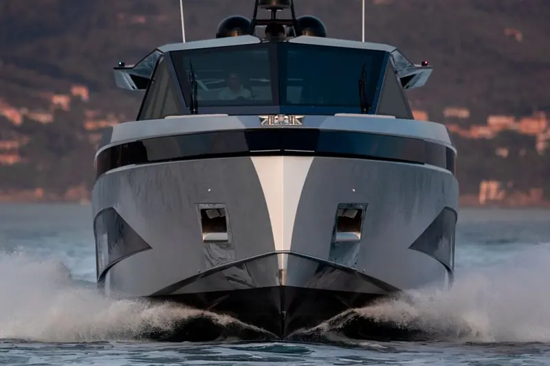 Head-on through a following sea at dusk, the nameplate visible on the bow and twin radar domes silhouetted above the windscreen.