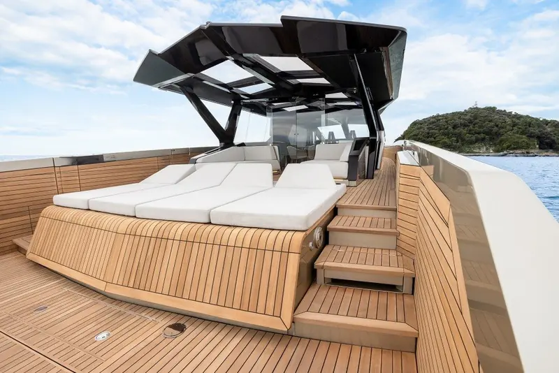 Foredeck sun pads under the open bimini frame, teak decking running forward to the anchor locker.