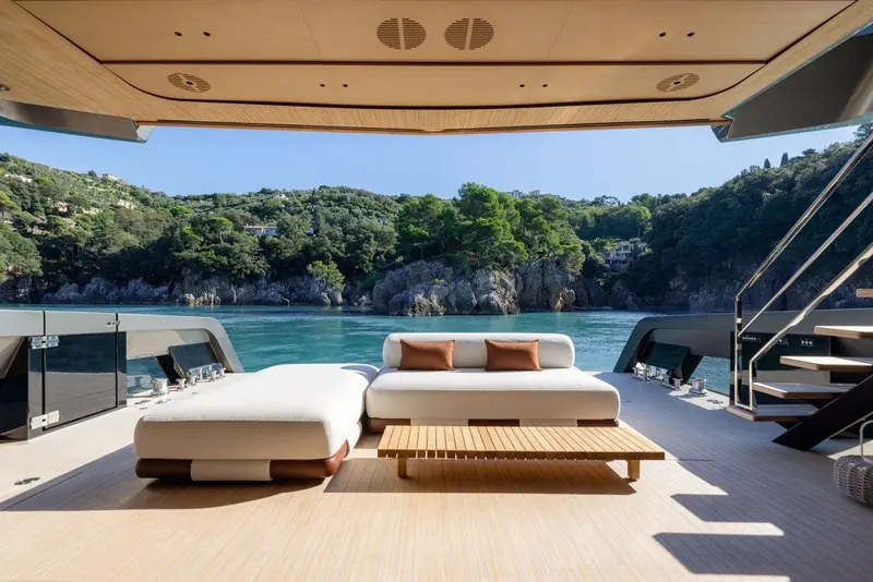 Forward lounge seating sheltered under the retractable bimini, rock cliffs and a stone stairway rising from the cove astern.