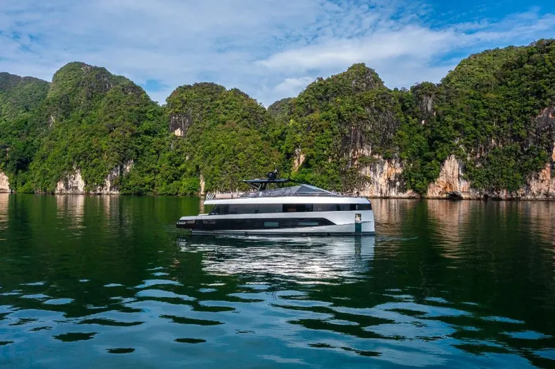 A distant view inside a green, cliff-walled cove that shows the yacht's scale against the surrounding coastline.
