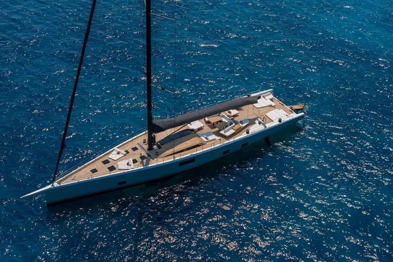 A near-vertical drone shot showing the full sail plan and hull length in one frame, wake bending away from the transom.