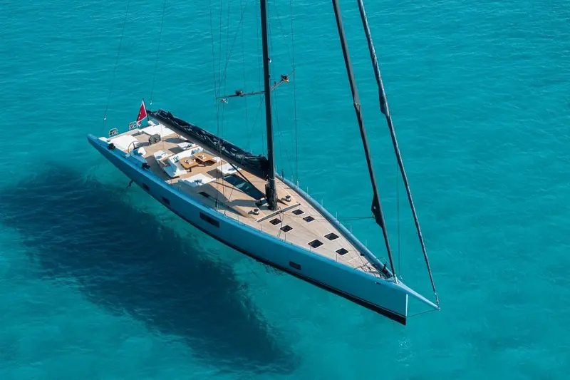 Running over shallow turquoise water, the hull's shadow visible on the sandy bottom beneath her.