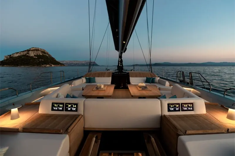 The aft cockpit at dusk, built-in bench seating around a folding table with the mast and boom overhead.
