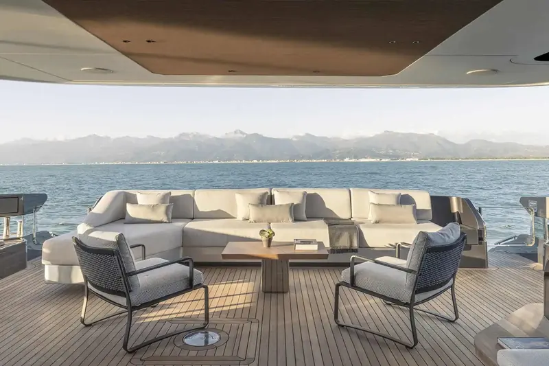 Aft deck seating at anchor off the French Riviera coast, the Alps visible across the bay in the evening haze.