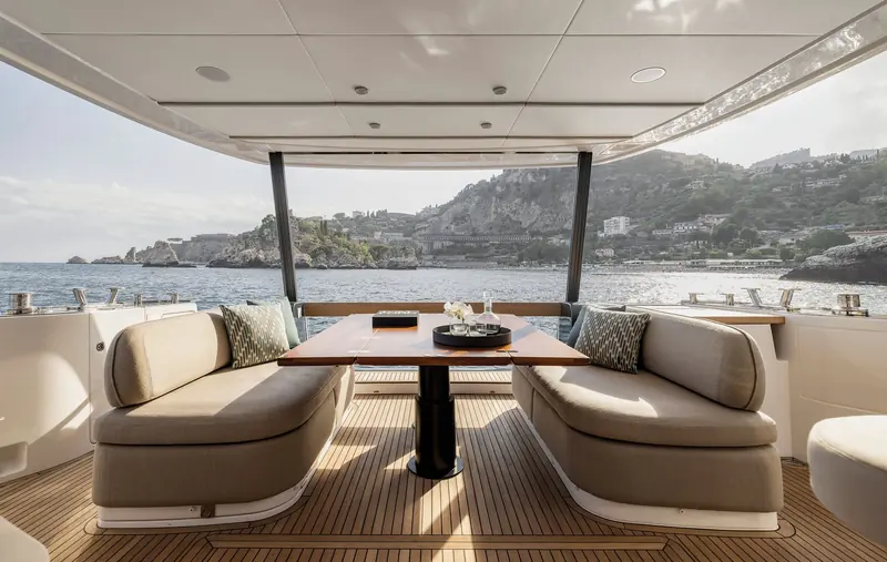 The covered cockpit dining table, shaded by the hardtop extension, looking out over the Sicilian coastline at anchor.