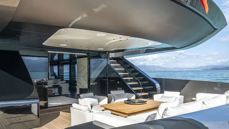 The aft cockpit dining table and lounge, the staircase up to the flybridge visible behind, with the Ligurian coast astern.