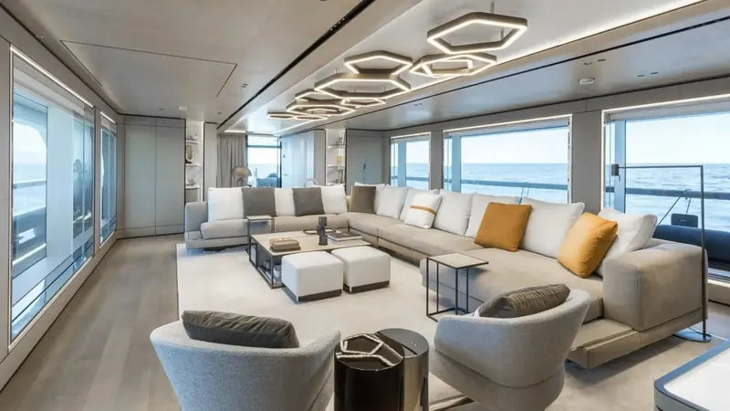 The main saloon aboard Akula, its hexagonal pendant lighting and full-beam glazing opening straight onto the sea.