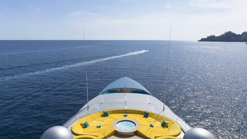 Looking forward from the bridge deck over the bow sunpad and Jacuzzi as a jet ski cuts a wake toward the coast.