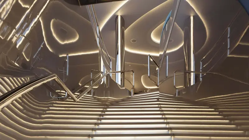 The main staircase, its polished stainless treads and backlit coving repeating in mirrored reflection up the stairwell.