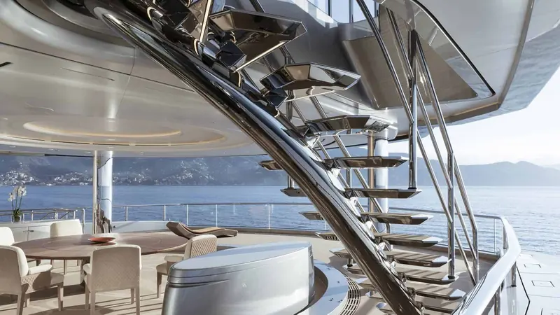 Aft deck dining beneath the sculpted staircase overhang, open to the water on three sides.