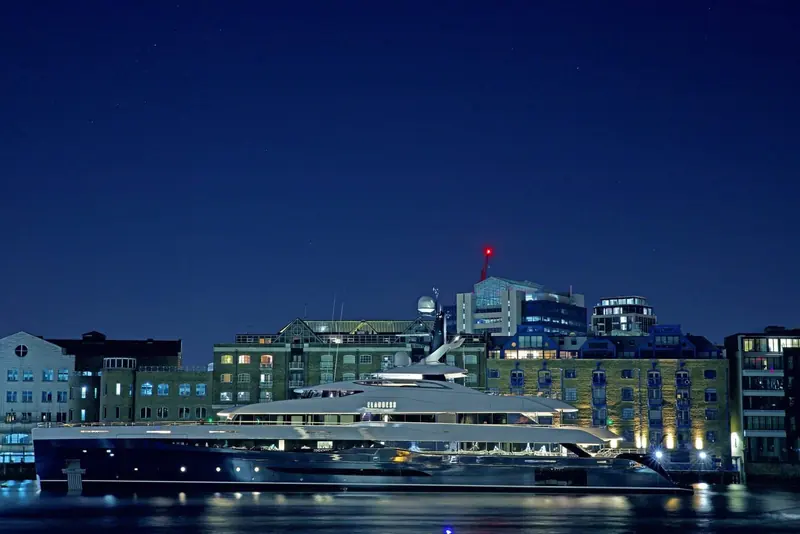 Alongside at night in a European harbour, city lights framing her long, dark hull.